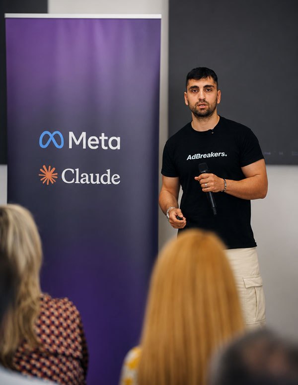 John Portalios speaking on stage beside a Meta and Claude banner